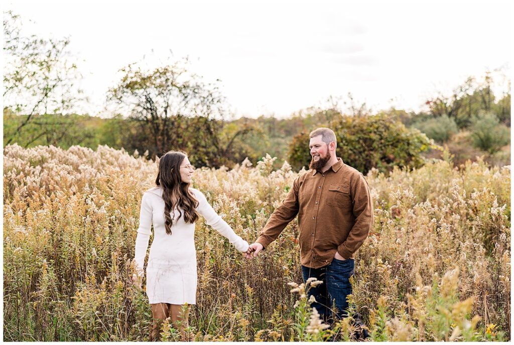 Couple walking through waist high grass in a field.