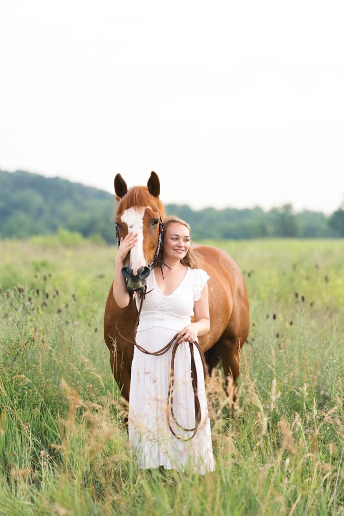 Girl standing with her hand on her horses's nose looking out over a field