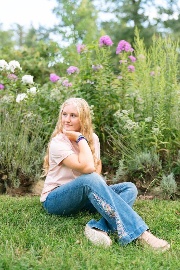 senior girl sitting in front of flowers looking over her shoulder