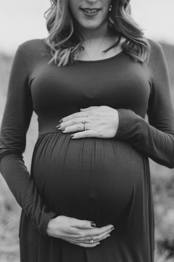 Black and white of baby bump with mom's hands around belly